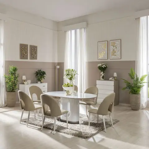 Symmetrical dining room with a sculptural white pedestal table, taupe fluted wainscoting, and matching white consoles styled