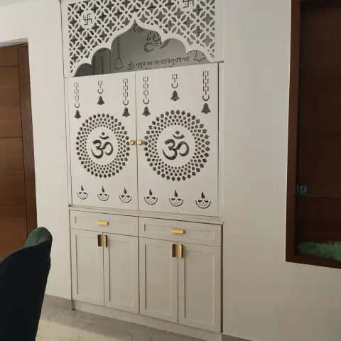Built-in pooja unit with laser-cut Om motif cabinet doors, a jaali screen mandir arch above, and brass drawer and door pulls.