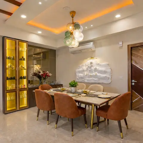 Dining room with a cove-lit ceiling in warm amber light, a bubble-cluster pendant chandelier, a backlit glass crockery