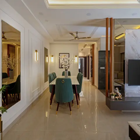 Open dining-and-living space with green velvet chairs around a marble table, a mirrored panel wall, and a marble-clad TV