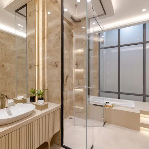 Beige marble bathroom with a frameless glass walk-in shower, a gold-trimmed reeded vanity with an oval countertop basin, and